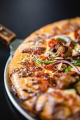 Close up of a supreme pizza with vegetables and sausage on a tray with handle 