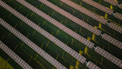 Aerial top view of solar panels arranged in diagonal rows on a green field, producing renewable...