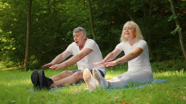 An active senior couple engages in stretching exercises in a peaceful park setting. Surrounded by trees, they enjoy the benefits of fitness at their age while fostering a healthy lifestyle.
