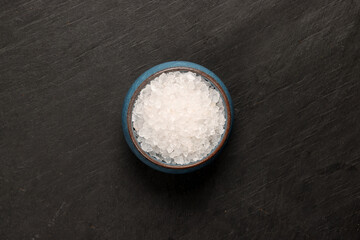 Sea rock salt granulate in small blue clay ceramic pot on a dark slate surface with a clean and neat appearance striking contrast vibrant spice top view flat lay