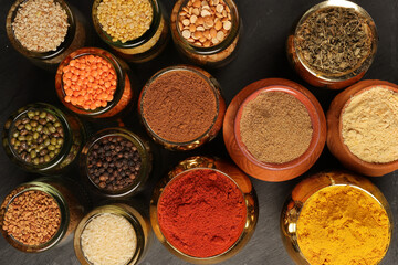 Overhead top view flat lay colourful array of spices herbs powder blue clay ceramic brass metal pot on dark black slate surface with a clean and neat appearance spice copy text space border frame