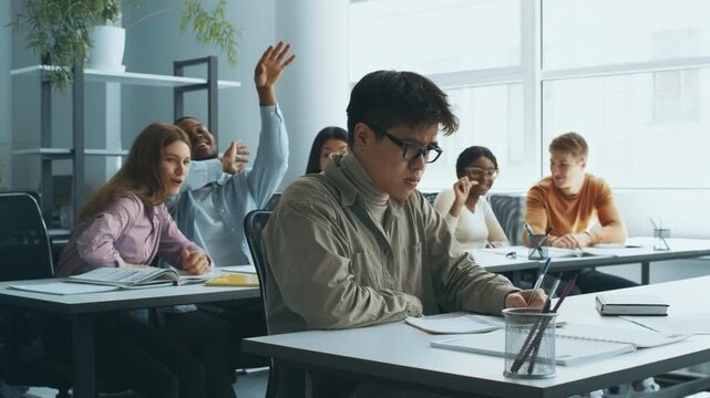 Group of diverse college students engaged in gossiping and bullying their classmate Asian guy wearing eyeglasses