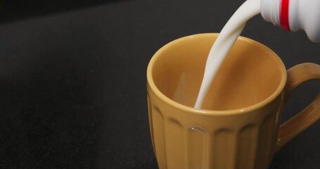 Pouring milk into a large orange glass in slow motion until it is completely full. - Powered by Adobe