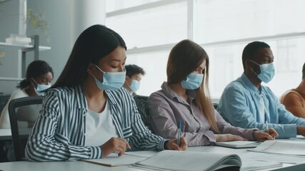 Diverse college students are focused on their studies, wearing masks while taking notes and collaborating in an interactive classroom environment, showcasing a commitment to education. - Powered by Adobe