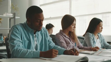 In a modern university classroom, diverse students actively participate in study sessions. They take notes and collaborate on academic assignments while surrounded by natural light.