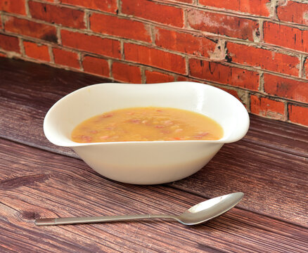 A plate of tasty and nutritious pea soup with smoked meat on a wooden table, a tablespoon nearby.