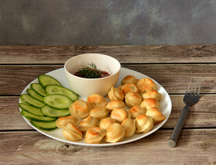 Fried dumplings on a large plate with pieces of fresh cucumber and spicy sauce on a wooden table, a fork nearby.
