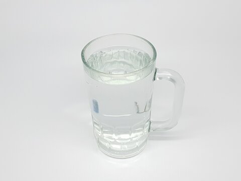 Transparent glass mug filled with fresh water placed on plain white background in studio lighting.