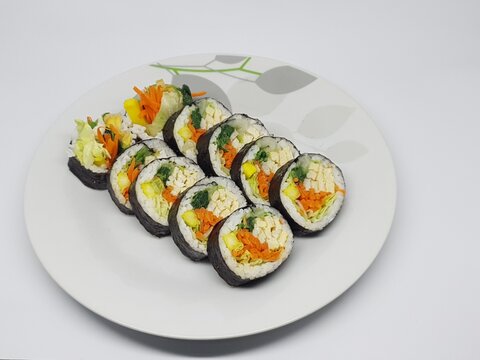 Korean-style kimbap sliced to show colorful fillings of carrot, spinach, and egg on a white background.