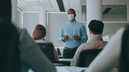 A diverse group of college students attentively listens to their instructor during a discussion in a modern classroom setting. The instructor, wearing a mask, presents key concepts effectively. - Powered by Adobe