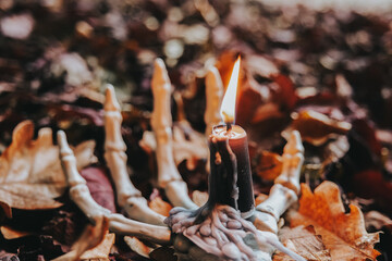 Halloween Candlestick. Burning Candle on Skeleton Hand with Autumn Leaves.Halloween wallpaper with bone hand and candle.