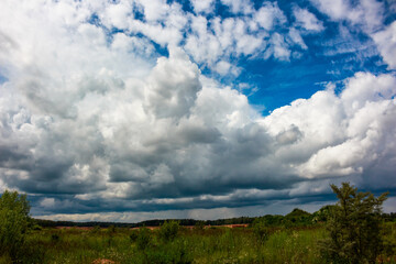Obraz premium Voluminous, turbulent clouds fill the wide sky, revealing bright blue patches. A grand, dramatic weather spectacle above lush fields