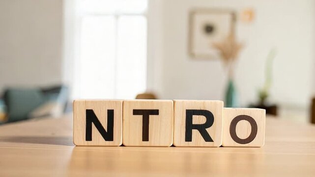 Four light wooden blocks spelling "NTRO" on a wooden table with a bright, blurred indoor background