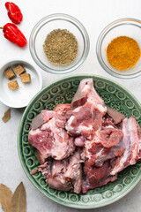 Overhead view of mise en place of ingredients and spices for cooking raw goat meat, top view of chopped goat meat being prepared for cooking	