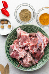 Overhead view of mise en place of ingredients and spices for cooking raw goat meat, top view of chopped goat meat being prepared for cooking	