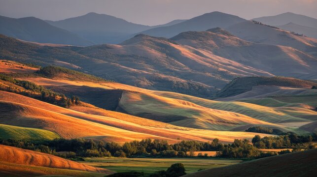 Golden and brown rolling hills with green trees in the foreground, under a clear blue sky with a few scattered clouds, creating a serene and picturesque landscape