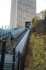 Naklejka premium An ascending funicular travels up a hillside beside a high-rise tower, representing connectivity, movement, and urban integration within a clean, minimalist setting