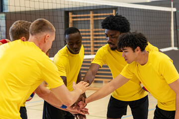 Diverse male volleyball teammates huddling and stacking hands on court with net, boundary lines