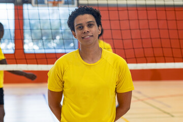 Hispanic male volleyball players standing on gym court by net wearing yellow jerseys, shorts