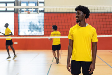 Diverse male partners in yellow shirts playing volleyball on court near net, copy space