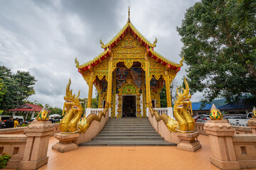 The ordination hall with a golden Naga staircase at Wat Phra That Doi Kham in Chiang Mai showcases...