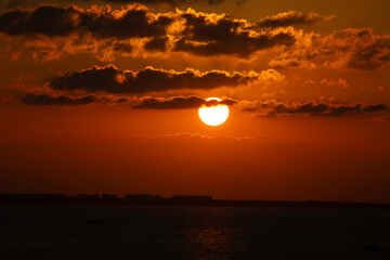 Obraz premium Isla Mujeres, Cancun, Mexico - The sun is setting over the ocean, casting a warm glow over the water. The sky is filled with clouds, creating a serene and peaceful atmosphere