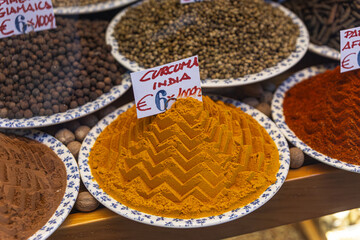 A vibrant display of spices in a Venice shop window, featuring a mound of bright orange turmeric powder marked 
