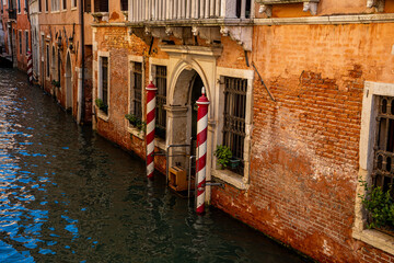 A weathered brick canal house facade in Venice, featuring an arched water entrance, barred windows,...
