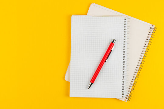 Notebooks and a red pen on a bright yellow background for study