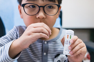 Asian child holding flu and COVID-19 test kit showing positive result for Influenza B. Health concept for virus infection, medical care, pediatric illness, and home disease detection.