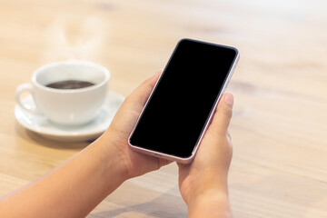 Person holding a smartphone in one hand while enjoying a cup of coffee at a cafe table in the morning atmosphere