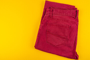 Stylish red jeans folded neatly on vibrant yellow background