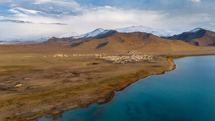 Aerial view of the snow-capped Pamir Mountains in Tajikistan, showing vast open plateau and dramatic peaks under a blue sky in remote Central Asia