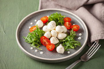Salad with arugula, mozzarella and tomatoes in a plate on the table