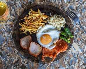 A hearty breakfast plate featuring fried eggs, bacon, fried potatoes, tomatoes, rice, and pickles, served on a decorative plate.