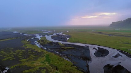 Icelandic streams twist on their journey through glaciated valleys, volcanic rock and vibrant mossy green flatlands to the sea. Drone aerial reveal horizon.