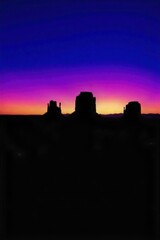 Fototapeta premium Vast desert landscape at dusk, with dramatic rock formations silhouetted against a gradient of orange and purple sky. A vast desert landscape at dusk. Dramatic, sculptural rock formations are