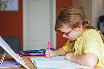 Cute elementary school girl writing in her workbook and doing school homework. Focused child learning and studying indoors. Concept of education, childhood, home learning.