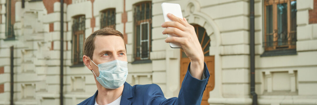 Young caucasian male taking a selfie wearing a mask in urban setting during daytime. - Powered by Adobe