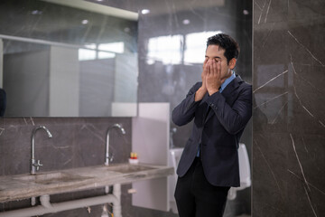 Stressed businessman covering face in office bathroom sink