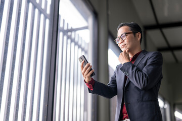 Pensive businessman using smartphone near office window