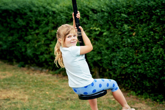 Happy kid girl rids on zip line swing outdoor game play equipment on playground. Child having fun outdoors. Preschool child swinging on summer day. Activity with children.