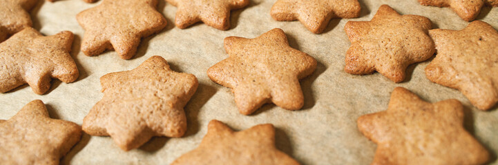Freshly baked star-shaped gingerbread cookies cooling on parchment paper in a rustic kitchen setting.