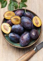 Fresh ripe plums in bowl on wood surface
