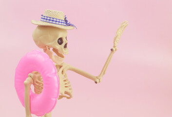 Human skeleton in hat with inflatable ring on pink background. Funny Halloween concept.