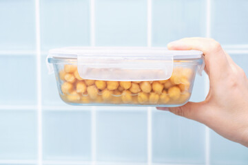 Hand holding glass container with chickpeas close up on blue tile background.