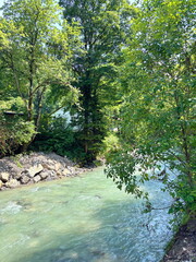 Amazing view of the Partnach mountain river carrying its waters overcoming stone barriers against the background of coastal trees of the mountain forest on a clear sunny day.
