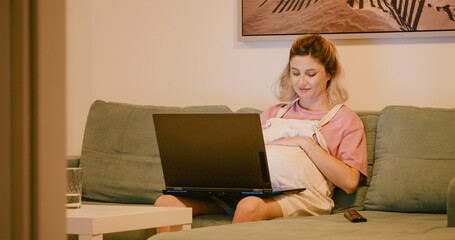 Pregnant vlogger editing content on laptop sitting on the sofa. Mom to be answering messages on social media.