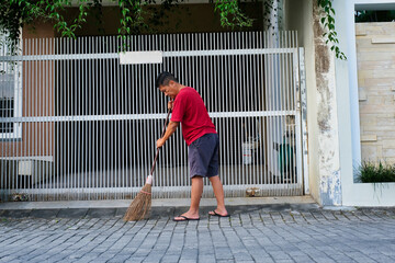 Man sweeping up the front yard with broomstick