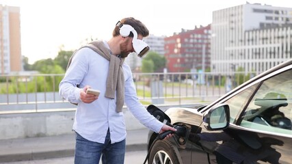 A man wearing a VR headset connects an electric vehicle to a charging station while holding a smartphone. - Powered by Adobe